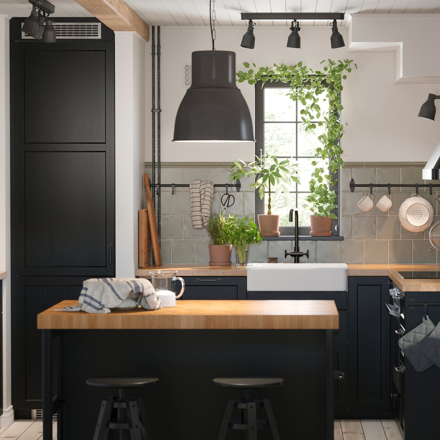 Et lille køkken med sorte LERHYTTAN køkkenlåger og en køkkenø over øen hænger en pendellampe.