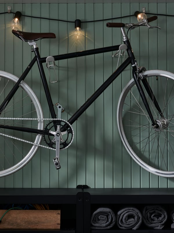 Væg med en cykel, der hænger på kroge, en tændt lyskæde, der hænger langs loftet, og en reol nedenunder.