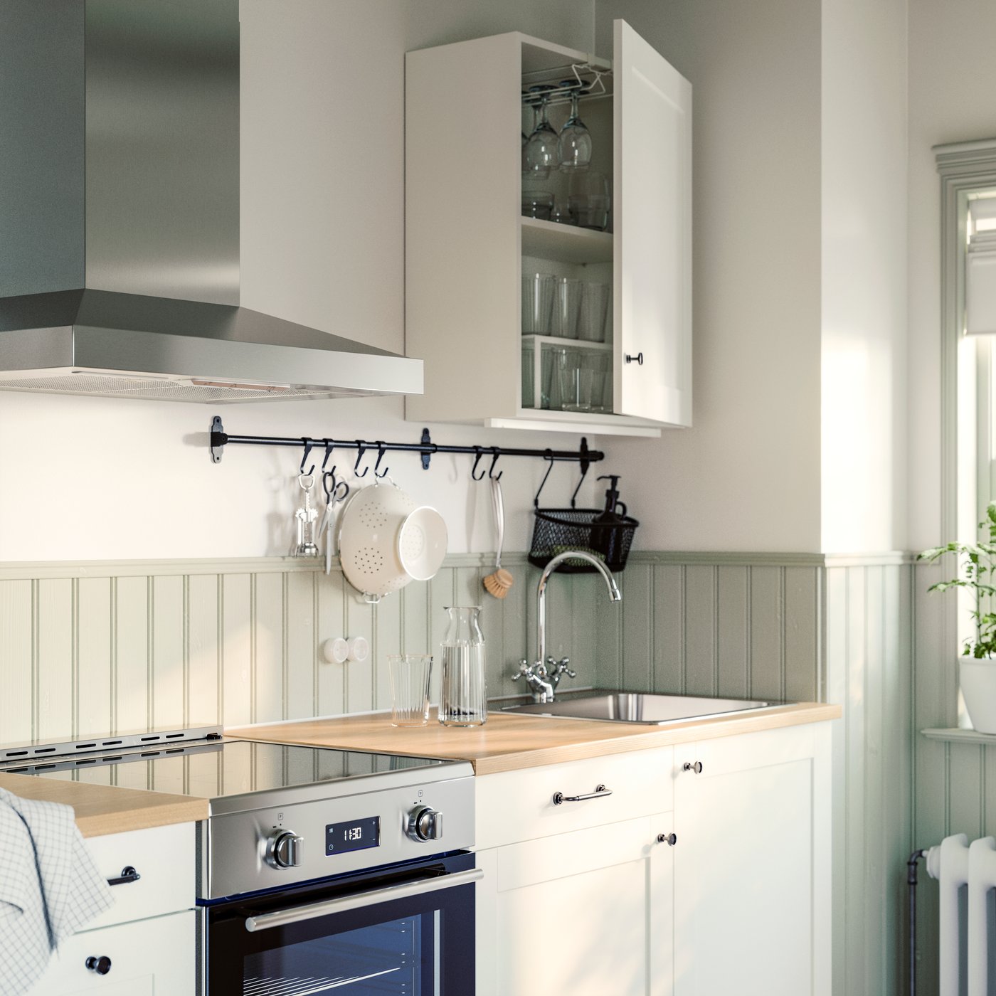 Une petite cuisine KNOXHULT blanche dispose d’articles ÖRMINGE avec une table de cuisson à induction et une hotte murale VINSTGIVANDE.