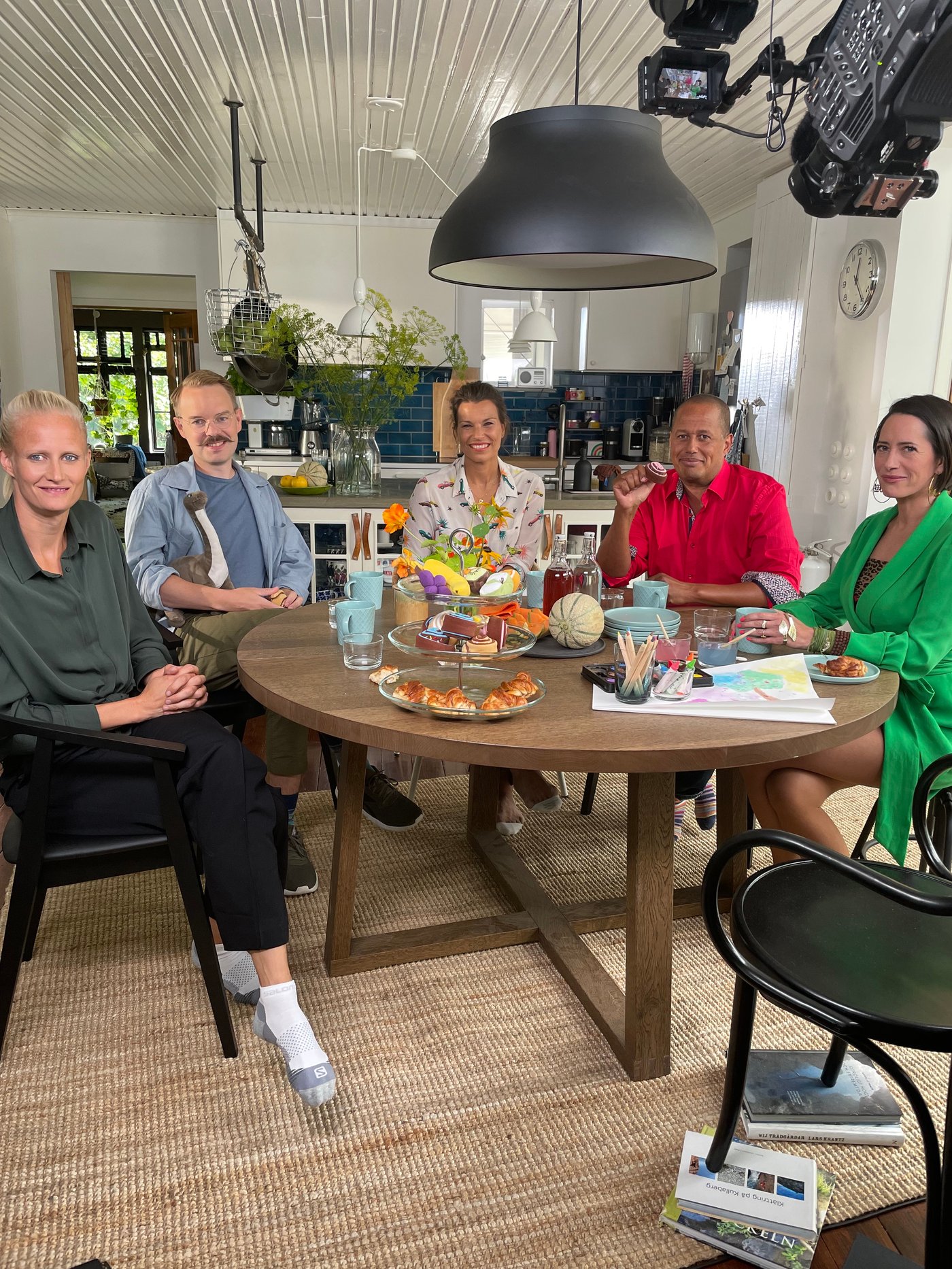 Četiri osobe za trpezarijskim stolom gledaju u kameru tokom snimanja.