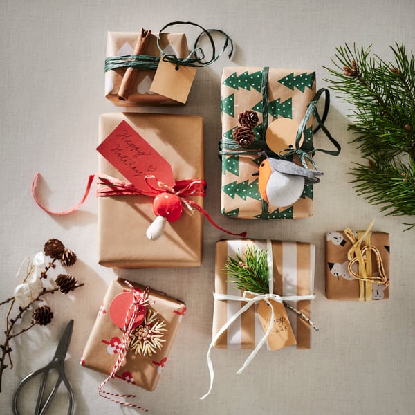 Six gifts wrapped in VINTERFINT wrapping paper, personalised with tree ornaments, a cinnamon stick and pine cones.