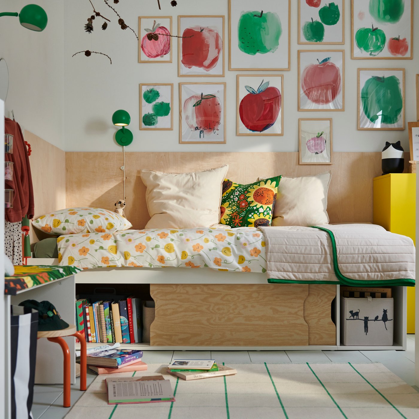 Um quarto com uma cama KLIPPUGGLA branca com arrumação em baixo, vestida com roupa de cama e almofadas florais e coloridas.