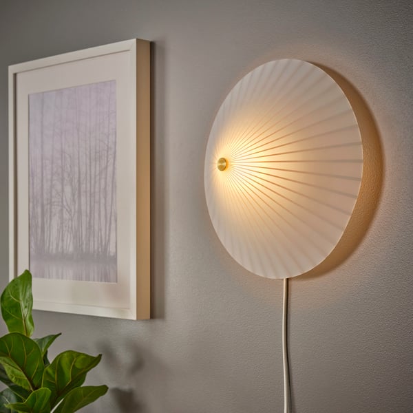 A stripe pattern/white glass RORKULT wall lamp is mounted on a wall near a painting in a frame which is also on the wall.