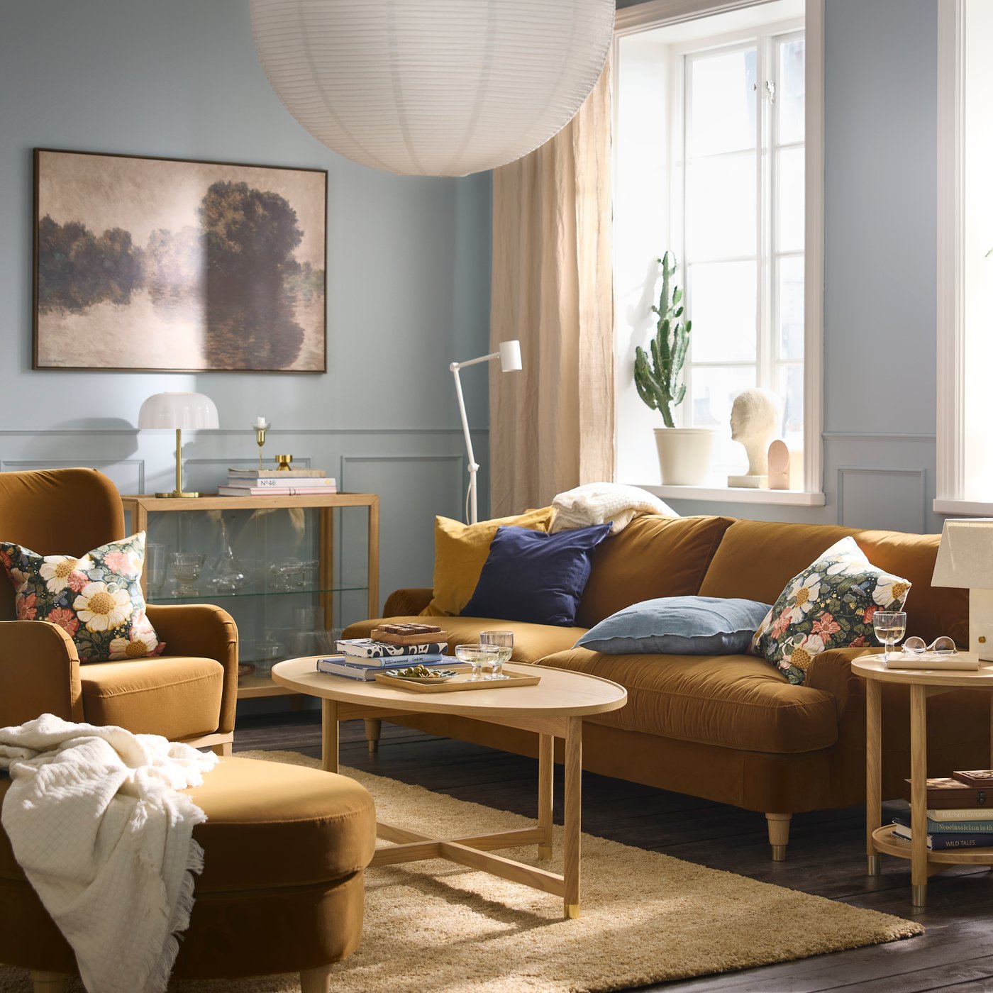 A softly sunlit living room with a VALNÄS sofa, floral-pattern cushions, a VALNÄS footstool, and a coffee table.