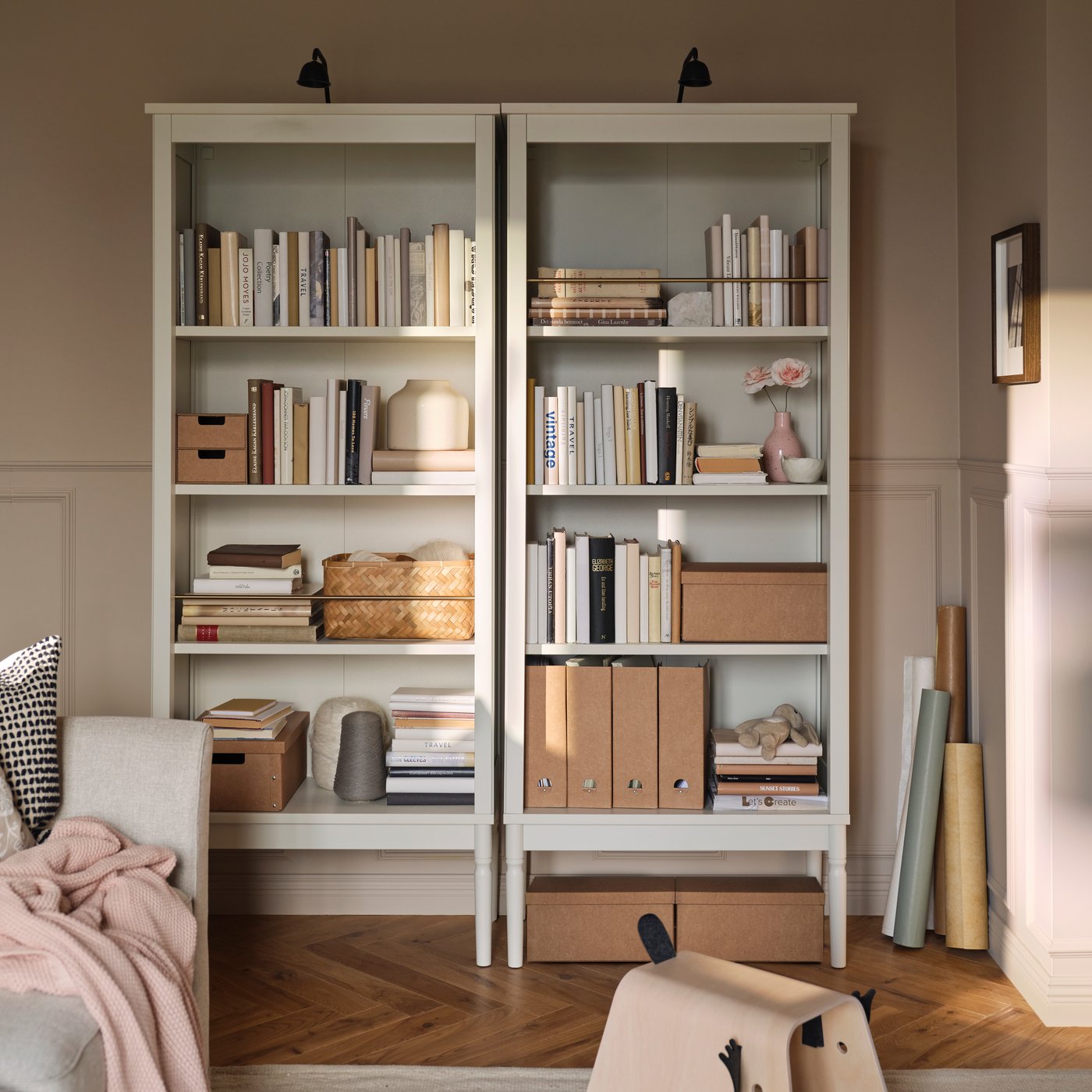 Blick auf zwei FÄRJKARL Bücherregale mit Büchern, GÄRDESGÅRD Zeitschriftensammlern und Boxen auf den Böden. An ihrem oberen Rand sind TVÄRDRAG Schrankbeleuchtungen befestigt.