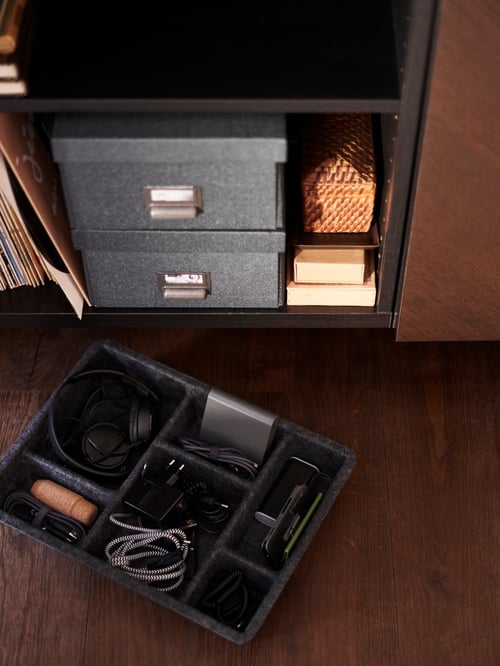 Two black shelves, the bottom shelf has dark grey storage boxes and records on it. A RAGGISAR tray is on the floor in front.