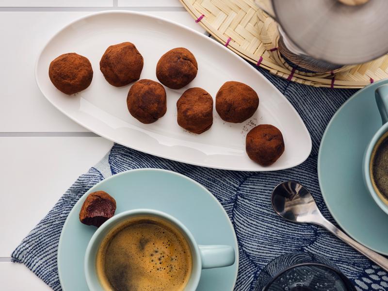 Chocolate truffles with coffee flavor on a small plate next to a cup of coffee.