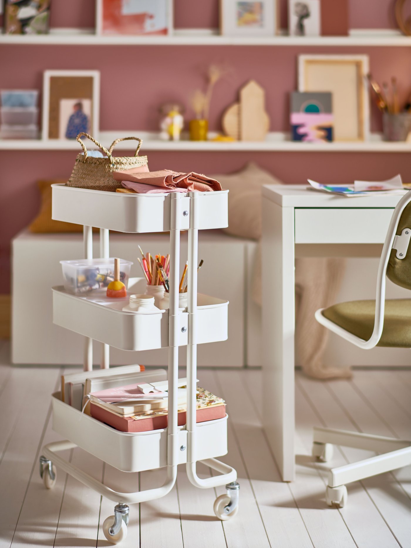 Una habitación con un carrito RÅSKOG blanco con artículos escolares al costado de un escritorio infantil. 