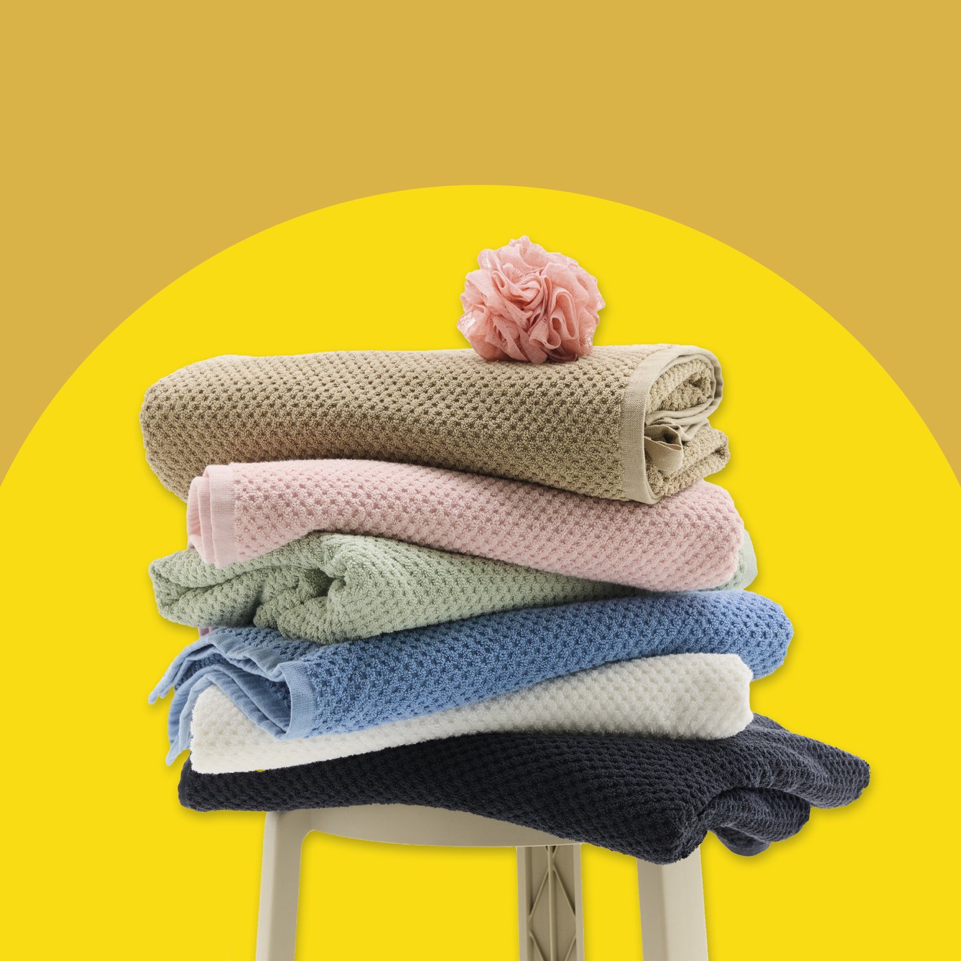 Various bath towels stacked on a stool on a yellow background.