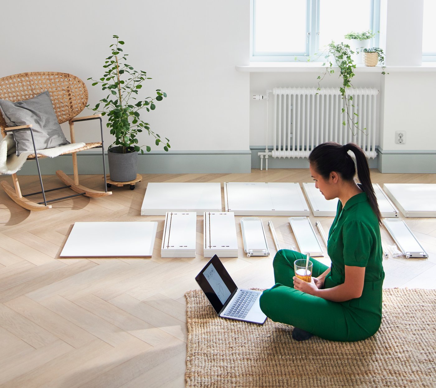 Person sidder i en stue med usamlet IKEA møbel på gulvet og med en computer foran sig.