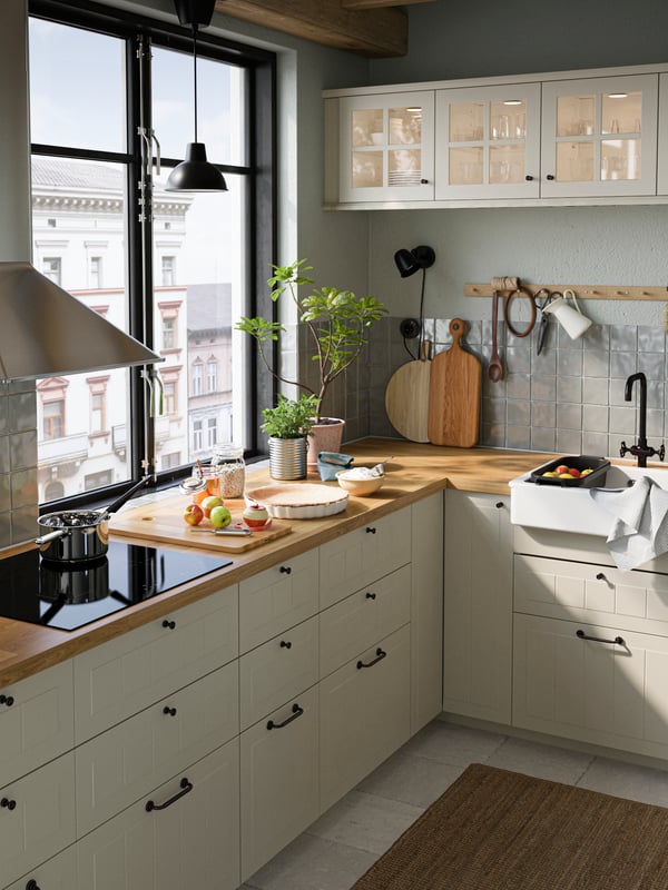 A kitchen with beige drawer fronts and glass doors, oak effect SÄLJAN worktops, an induction hob and a black pendant lamp.