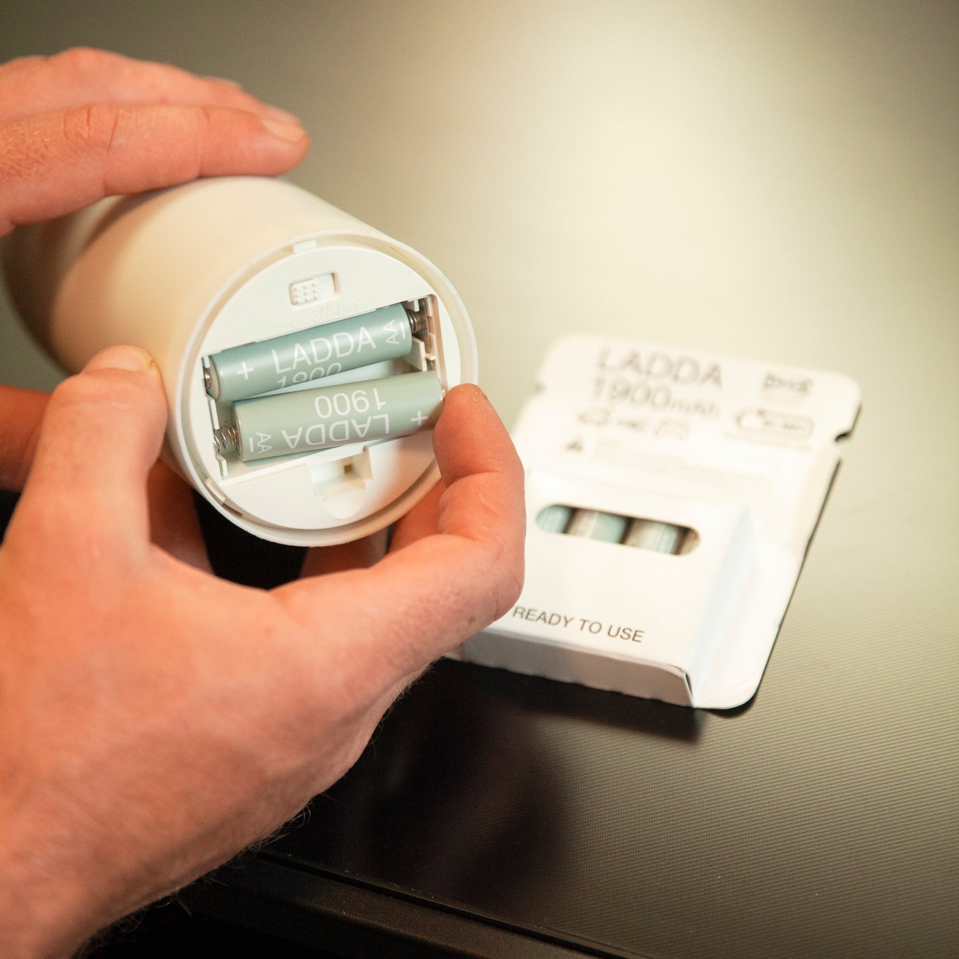 A man puts batteries into a ÄDELLÖVSKOG LED block candle.