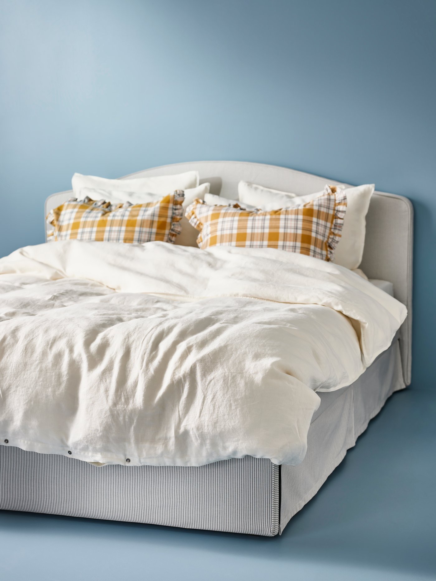 A RAMNEFJÄLL bed with striped fabric is neatly made with patterned pillows and a light-coloured duvet cover.