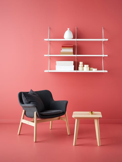 Red living room with dark grey armchair with four wooden legs, wooden side table, and white wall shelf combination.