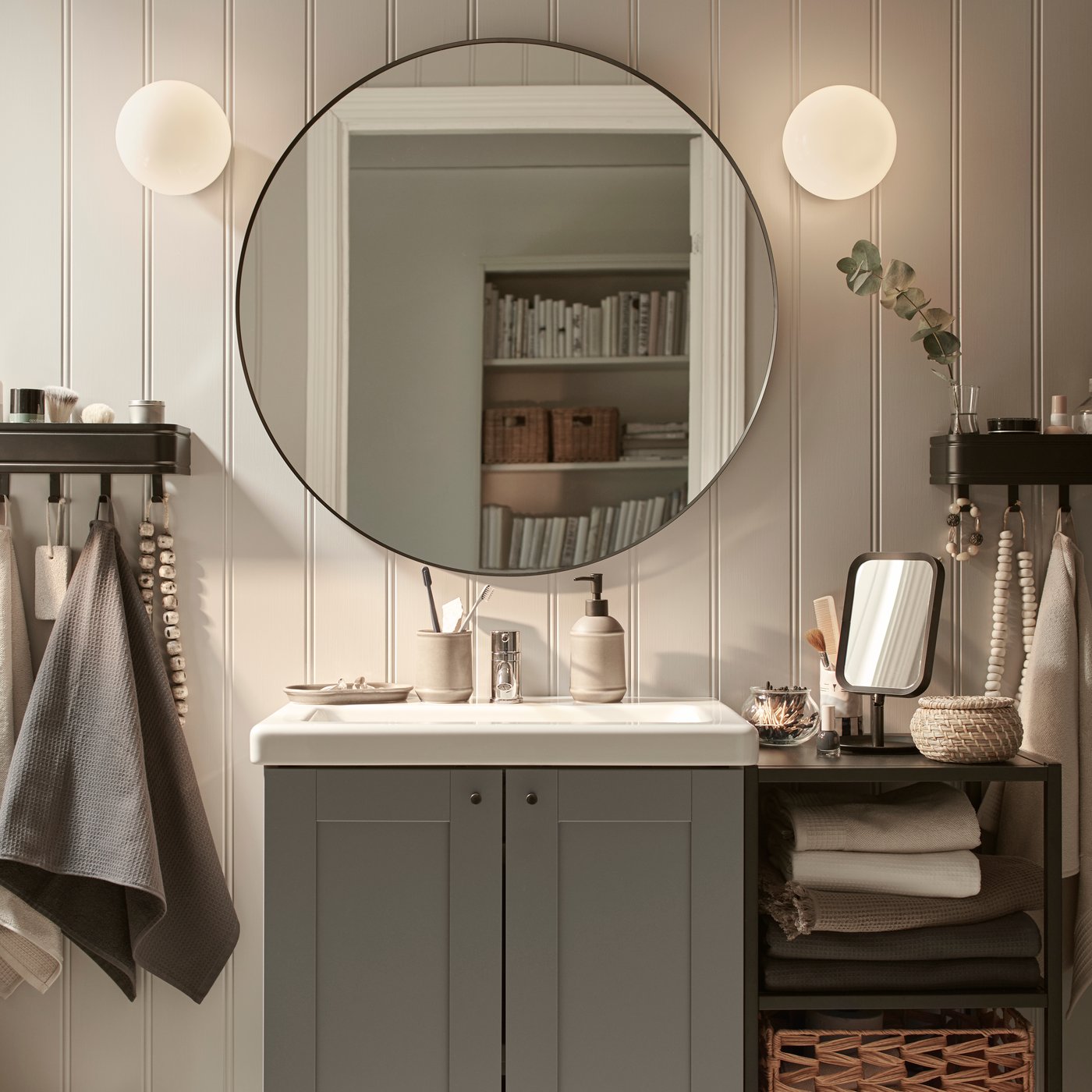 Okrągłe lustro LINDBYN wiszące nad szarą szafką umywalkową.