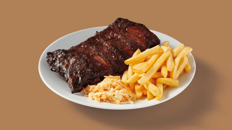 Assiette de ribs caramélisés avec frites dorées et salade de chou, servie au restaurant.