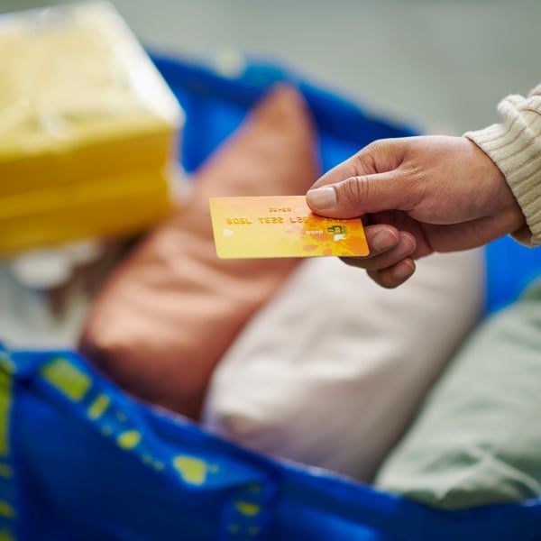 Osoba drži karticu za plaćanje iznad kese FRAKTA pune IKEA proizvoda.