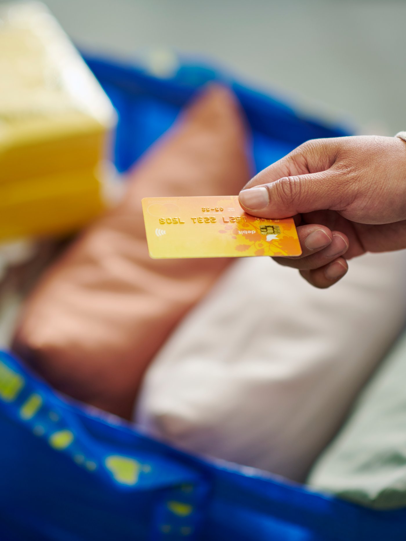 Oseba drži v roki plačilno kartico na IKEA vrečko.