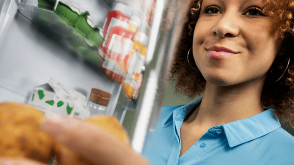A person is smiling while reaching into a refrigerator to pick up something up.