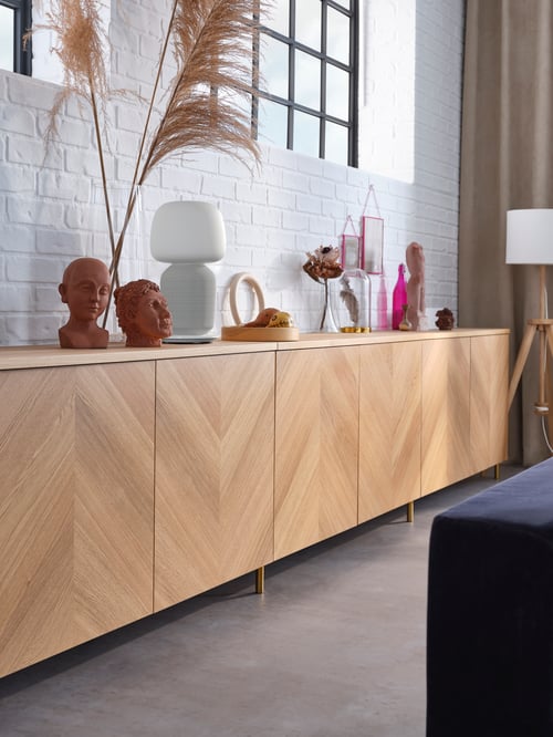 A modern living room featuring a storage combination with doors, a top panel, a transparent vase, and a floor lamp.