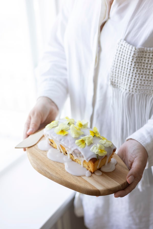 Someone holds a board with a citron cake on it, decorated with icing and pansies 