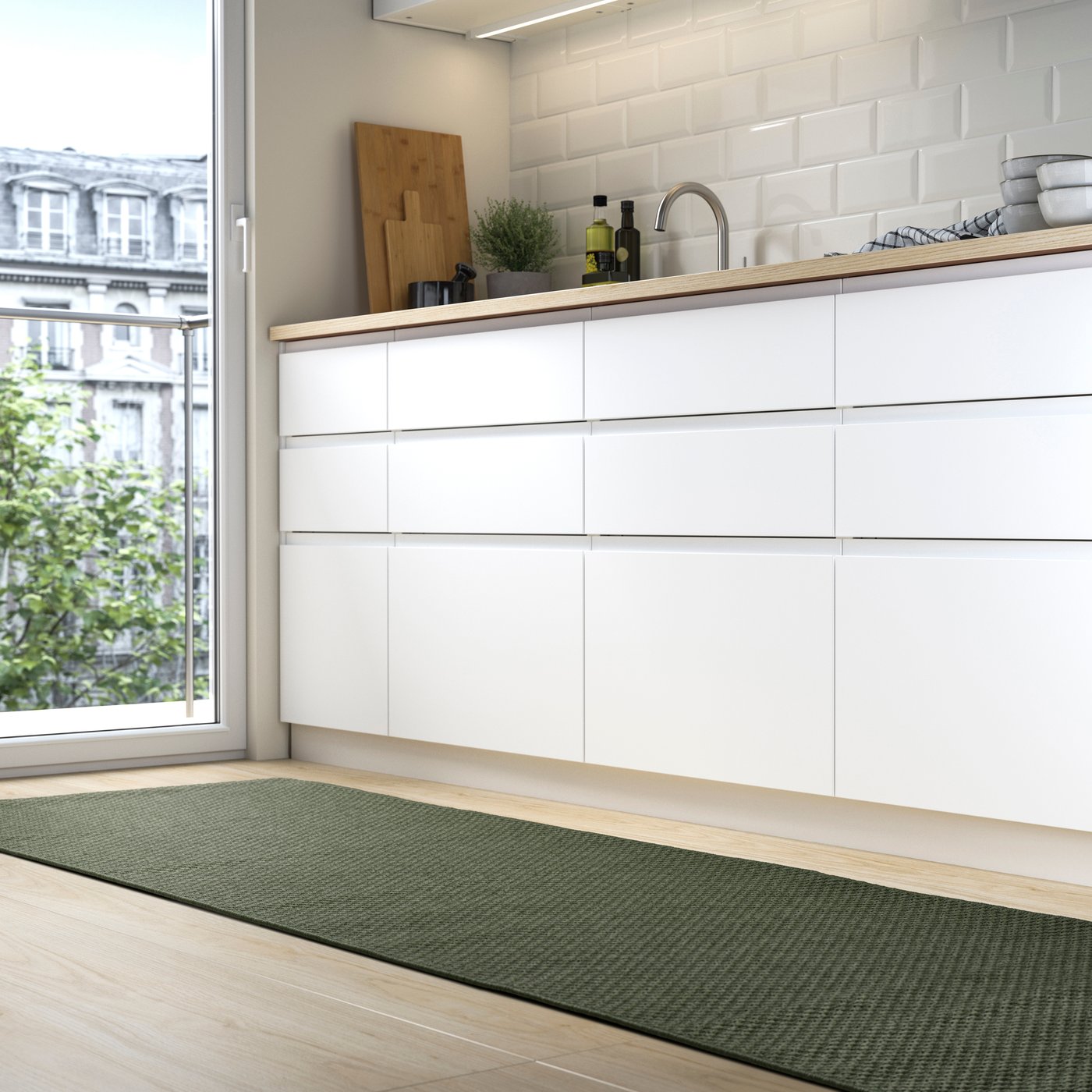 Ein grüner MORUM Läufer liegt vor einer modernen Küche mit weißen Fronten. Natürliches Licht fällt durch das Fenster.