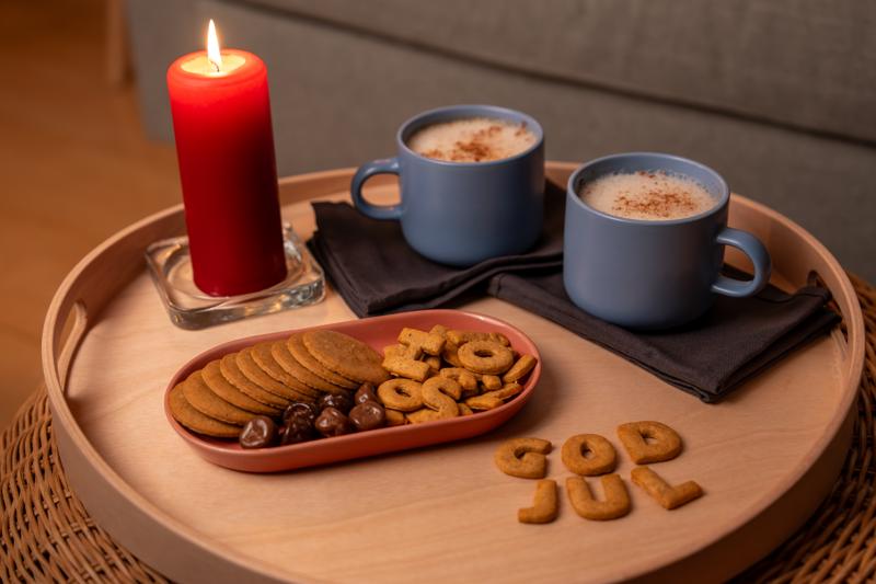 Zwei Tassen schwedischer Kakao mit einem Keksteller und einer roten Kerze auf einem Tisch präsentiert.