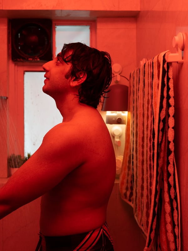 A man turns the water on in his shower. The lighting is red.