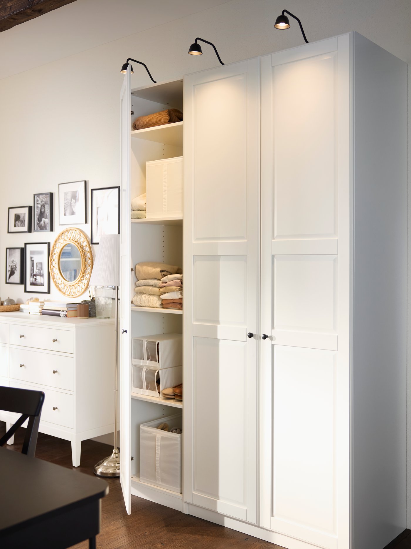 Combination of three PAX/TYSSEDAL wardrobes in white with one door open and a white chest of drawers in background.