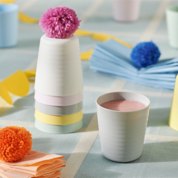 Various pastel coloured KALAS children’s mugs on a light blue check table cloth. One is filled with a pink smoothie.