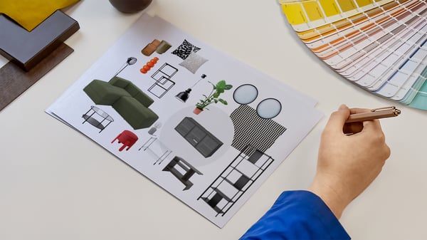Projektantka wnętrz IKEA prezentująca kartki z wydrukiem kolażu produktowego zaprojektowanego pomieszczenia. Obok na blacie leży wzornik kolorów i próbki materiałów.