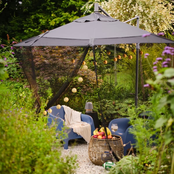 Pérgola en el jardín con sofás azules, una mesa y una guirnalda de luces.