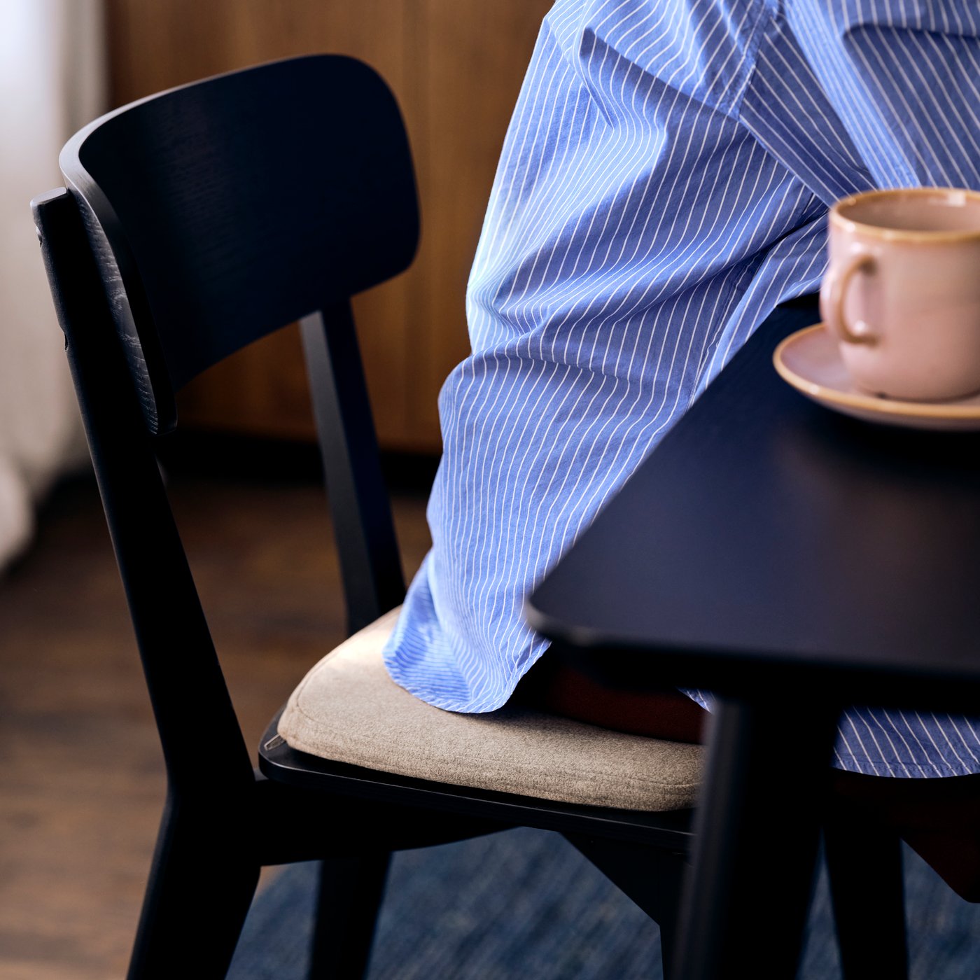 A person sitting on a LISABO chair in black, with an ÄLVGRÄSMAL chair pad in beige, and at a LISABO table in black.