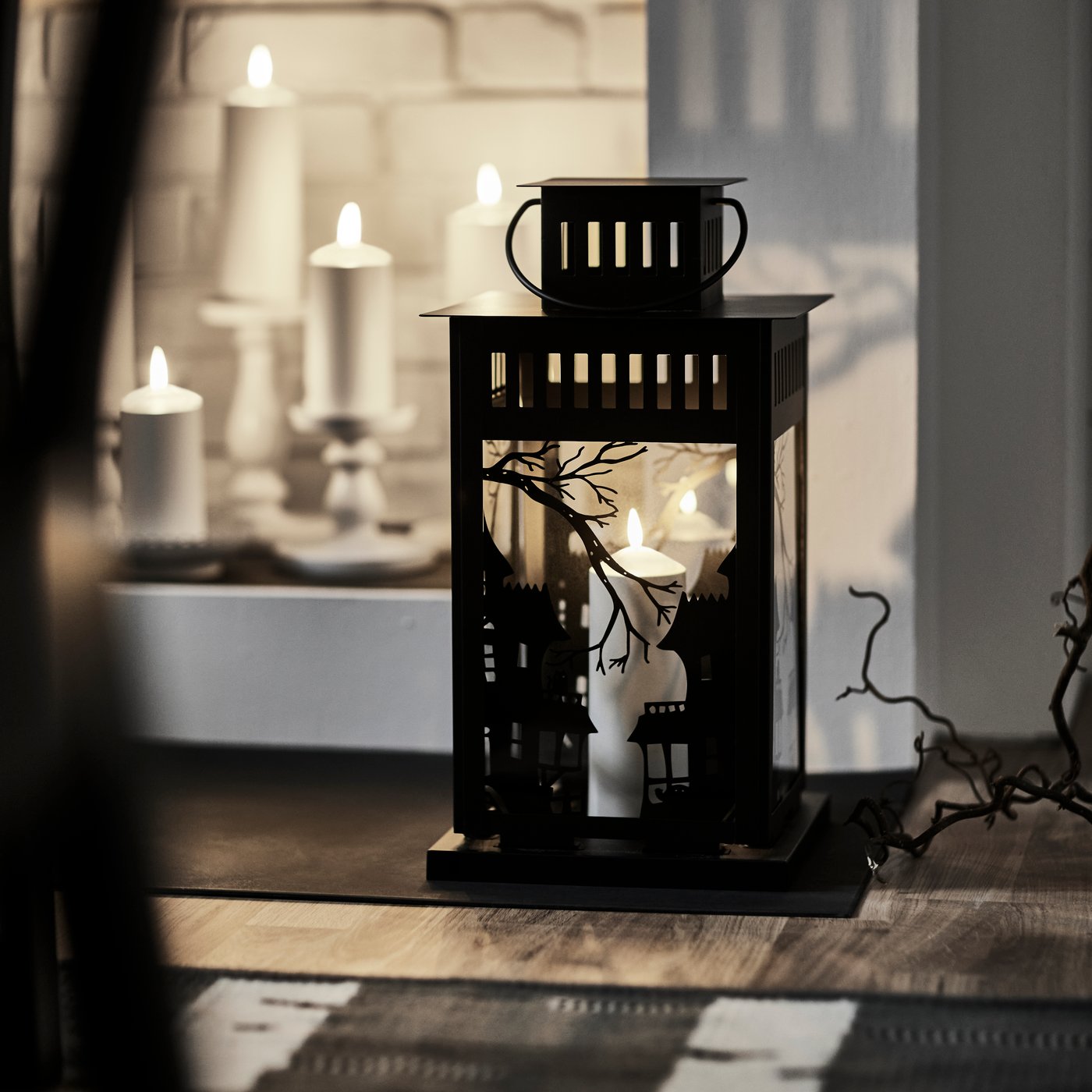 Czarna latarenka KUSTFYR stojąca na podłodze obok okna.