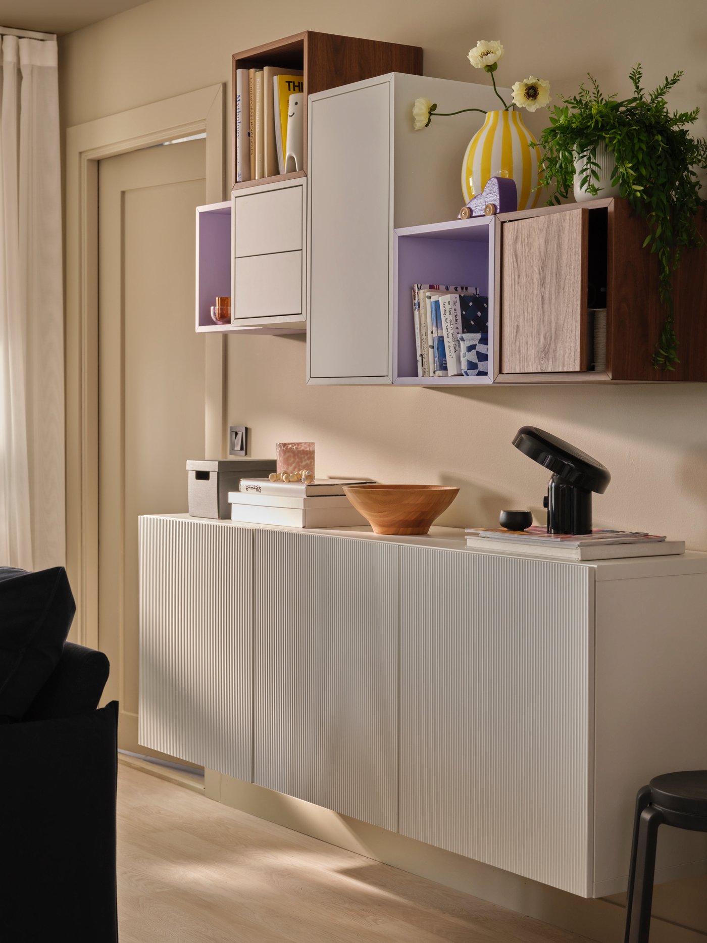 A softly sunlit living room with an asymmetric combination of EKET and BESTÅ wall cabinets, holding books and decoration.