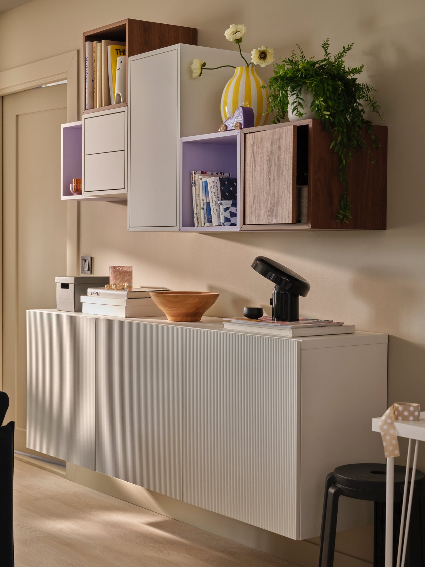 A softly sunlit living room with an asymmetric combination of EKET and BESTÅ wall cabinets, holding books and decoration.
