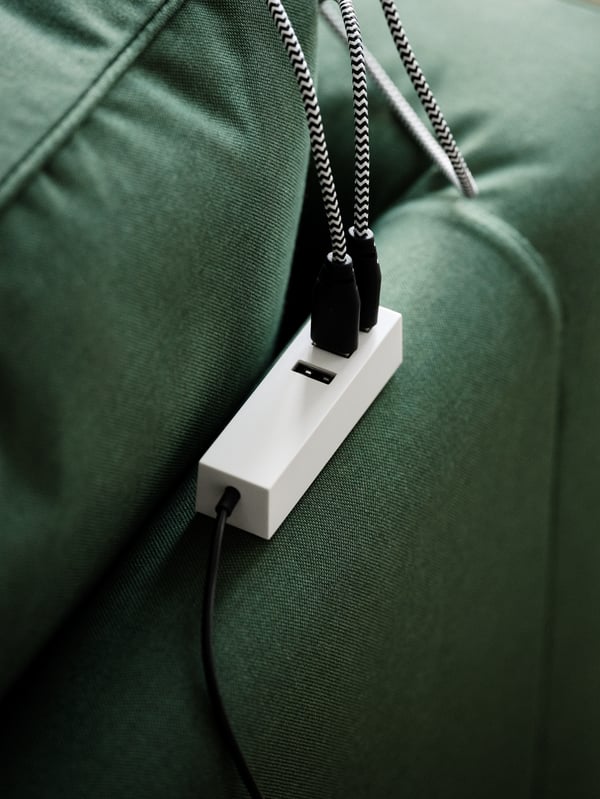 Un chargeur USB magnétique LÖRBY placé à l’arrière d’un canapé vert PÄRUP avec deux câbles qui y sont connectés.