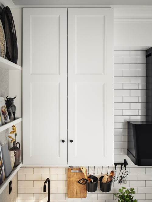 Zwei weiße AXSTAD Türen mit SKRUVSHULT Knöpfen an einem Wandschrank, daneben ein Regal mit Dekorationen.