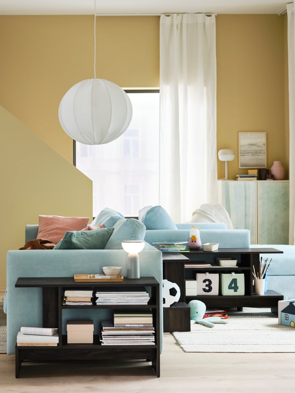 A BETTORP mobile lamp on a side table beside a light blue VIMLE 3-seat sofa bed that’s back-to-back with a chaise longue.