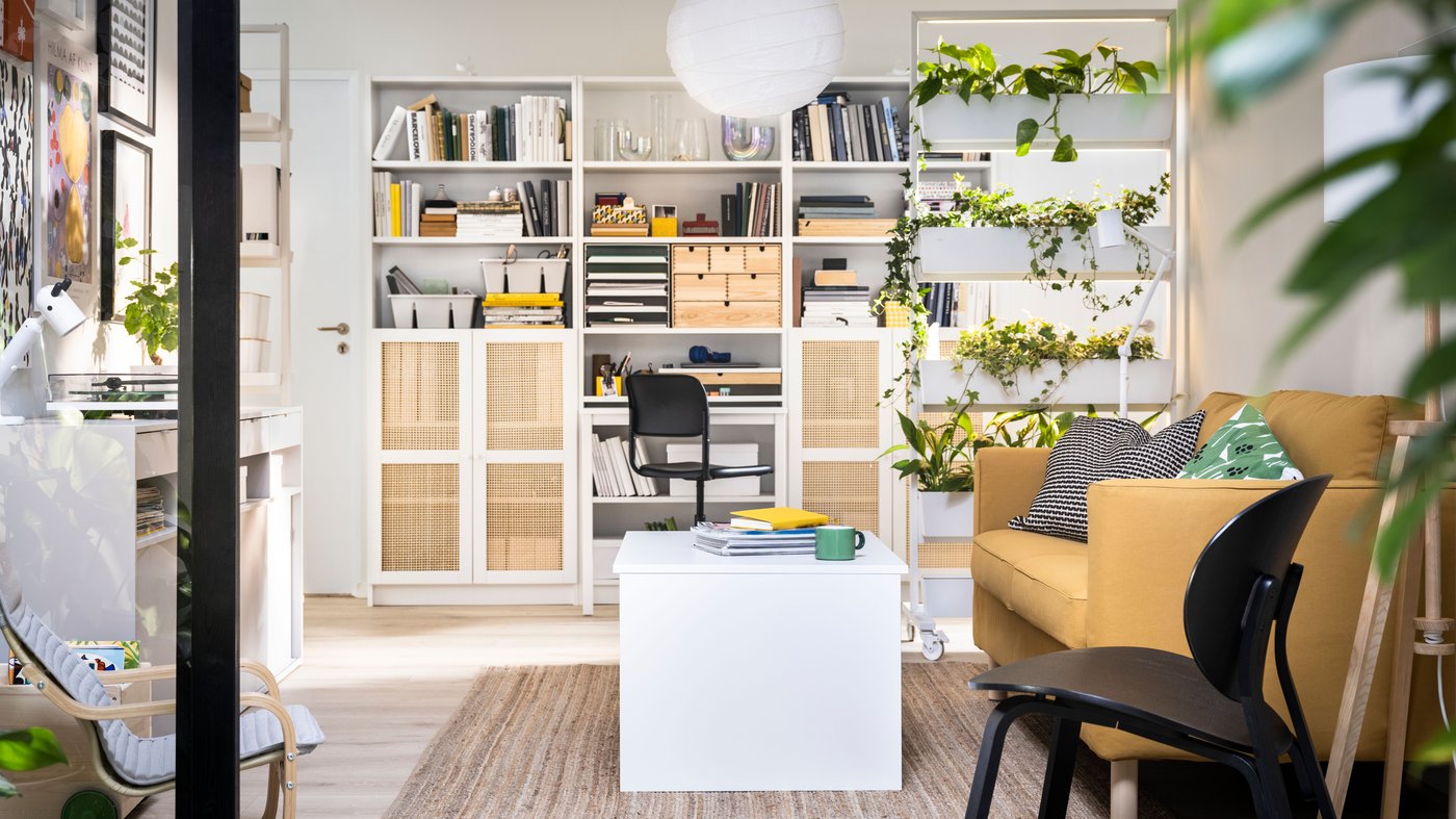 Een lichte woonkamer met een bruine bank, een open kast tegen de wand en veel natuurlijke accessoires