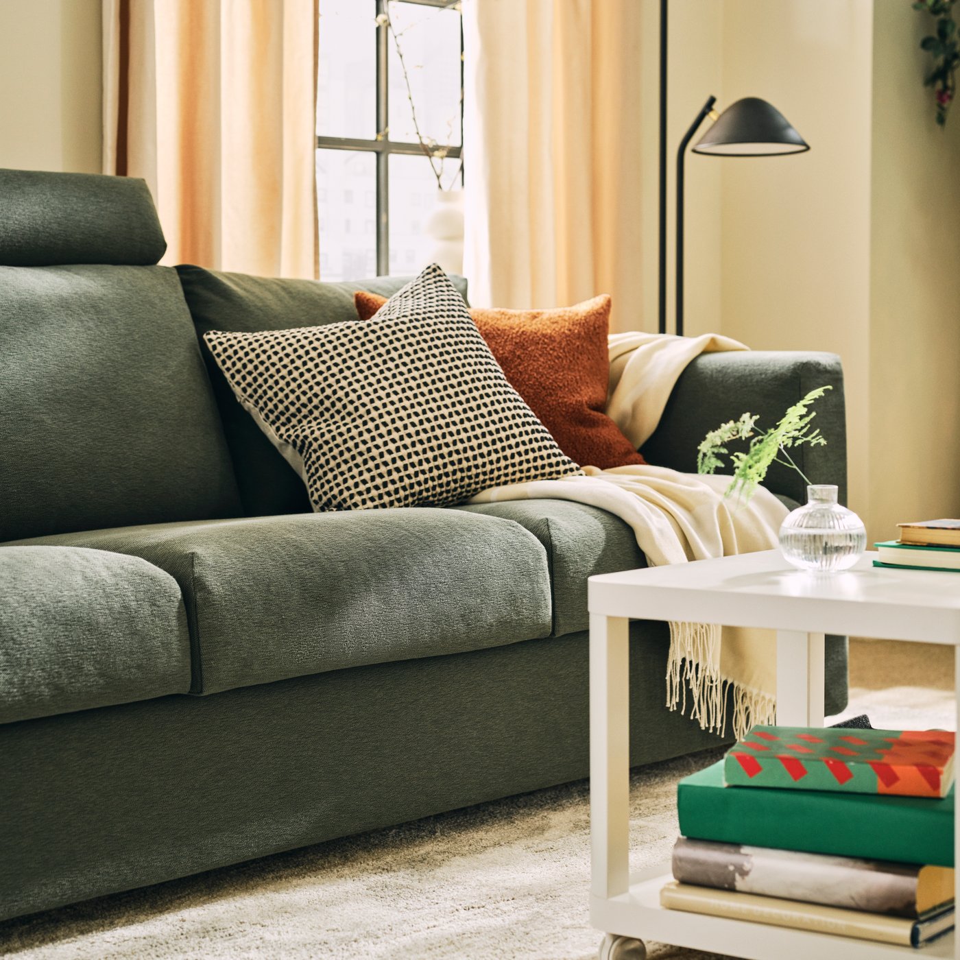 Part of a light living room with a grey-green VIMLE three-seat sofa next to a white TINGBY side table and a floor lamp.