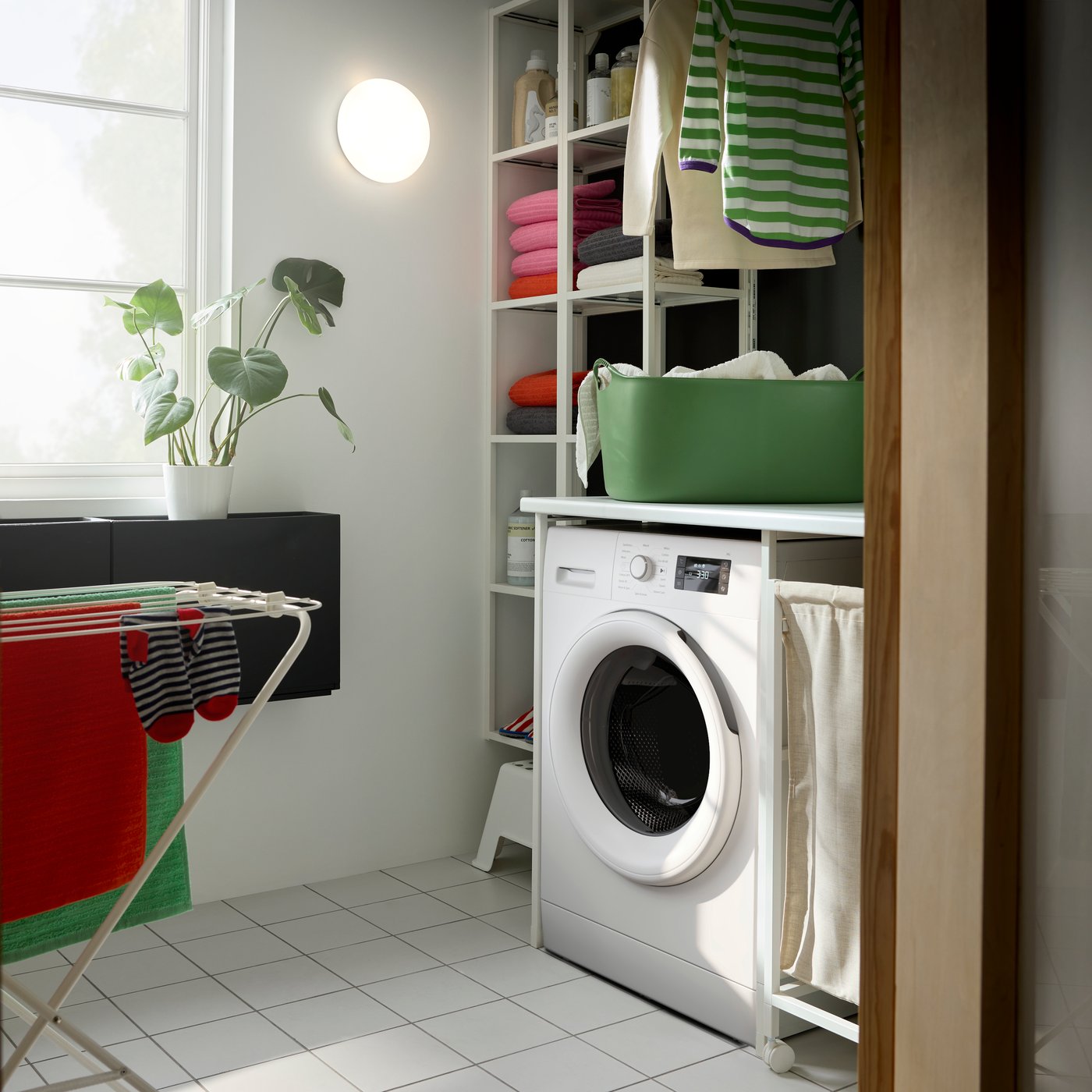 A white ENHET laundry combination with open storage and a washing machine. Green flexi laundry basket and a drying rack.