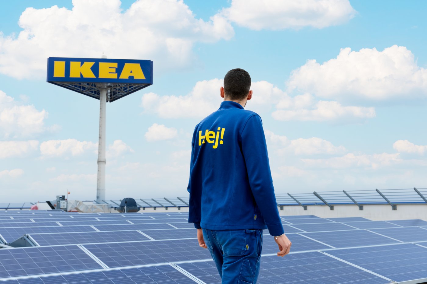 Сотрудник IKEA в рабочей форме идёт по крыше с солнечными панелями; на заднем плане видна вывеска IKEA.					