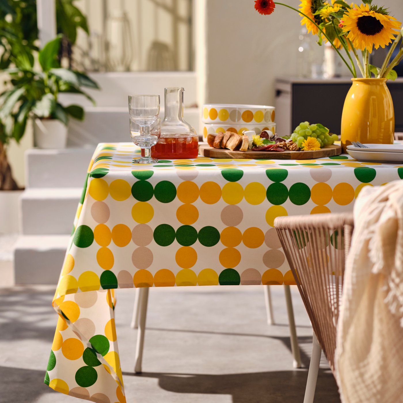 Letní kolekce BRÖGGAN, plná zářivých barev. Na obrázku je prostřený stůl a ubrus se vzorem kroužků v zelené, źluté, oranžové a béžové barvě.
