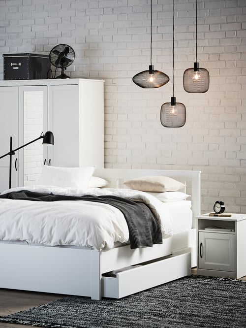 Bedroom with bed frame and mattress, bedspread, duvet, bedside table, flat-woven rug, three lampshades and a wardrobe.