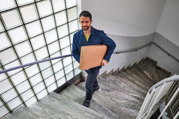 Un livreur IKEA portant un colis monte un escalier.