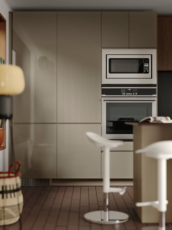 Kitchen cabinets with integrated appliances with VOXTORP high-gloss dark grey-brown fronts are mounted in a straight line.