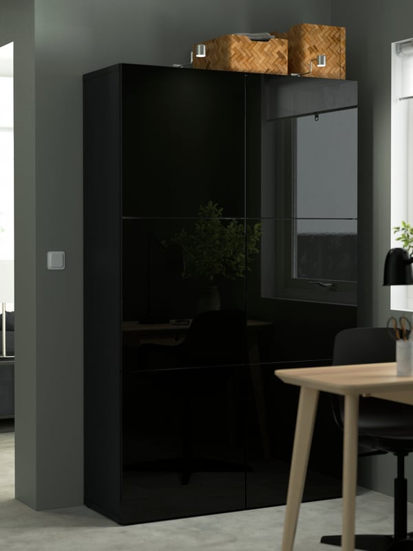 Une combinaison de rangement BESTÅ brun noir/selsviken brillant/noir avec des portes noires dans une salle à manger