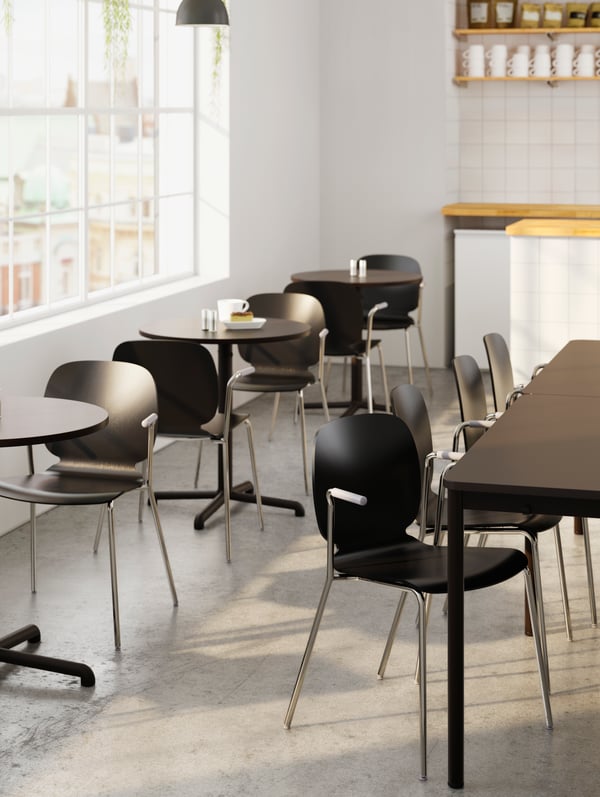 A group of dark tables with matching chairs next to several small round tables with chairs by a row of windows.