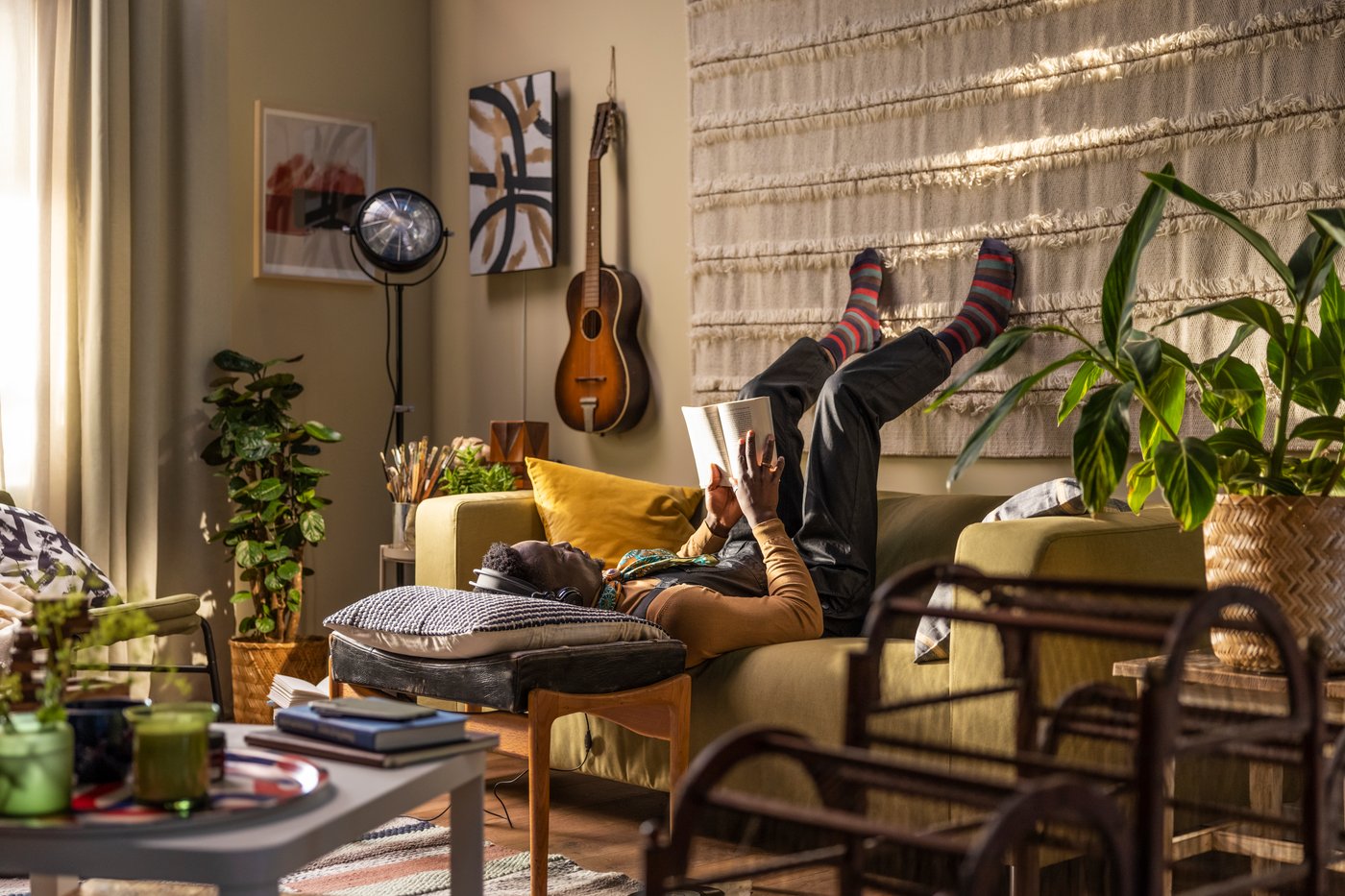 A person laying on a yellow sofa upside down and reading a book, his head on a pillow resting on a coffee table. A black bar at the top of the image with white text saying "Your home. On your terms."